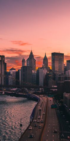 the city skyline is lit up at sunset with cars driving on the road in front of it