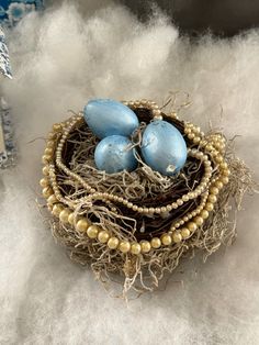 three blue eggs sitting in a nest on top of some white fluffy material with beads