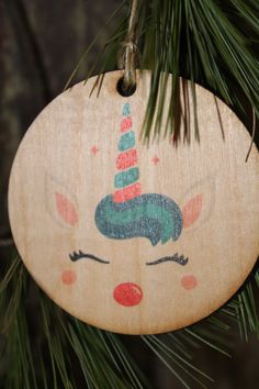 a wooden ornament with a unicorn face on it hanging from a pine tree