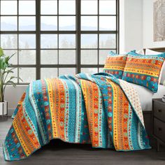 a bed covered in a blue and orange blanket next to a window