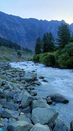 there is a river with rocks and trash on the bank in front of some mountains