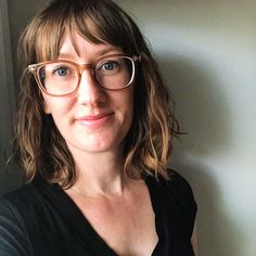 a woman wearing glasses standing in front of a wall