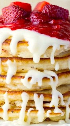 a stack of pancakes topped with strawberries and icing on top of a white plate