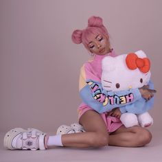 a woman sitting on the ground holding a hello kitty stuffed animal in her arms and wearing pink hair