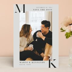 a couple sitting on a couch next to a vase with flowers and a photo frame