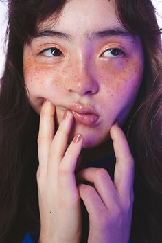 a woman with freckled hair and blue shirt holding her hand to her face