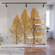 a living room with a large wall mural featuring yellow trees in the fall, along with a chair and bookshelf