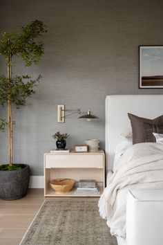 a white bed sitting next to a wooden table with a potted plant on top of it