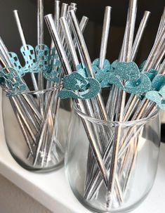 two clear vases filled with silver and blue decorative straws on top of a white counter