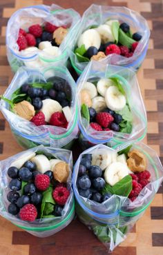 four plastic bags filled with fruit and veggies on top of a wooden table