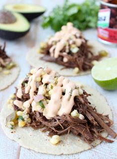 three tortillas topped with shredded meat, corn and avocado on a table