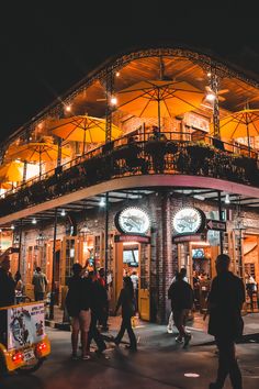 people are walking around in front of a building at night with lights on the roof