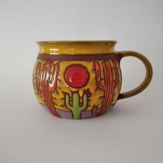 a yellow and red mug with cactus designs on it's side, sitting on a white surface