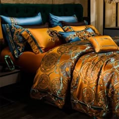 a bed covered in gold and blue comforters with pillows on the headboard next to it