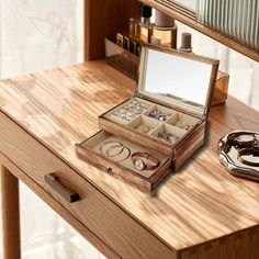 an open jewelry box sitting on top of a wooden table next to a cup and mirror