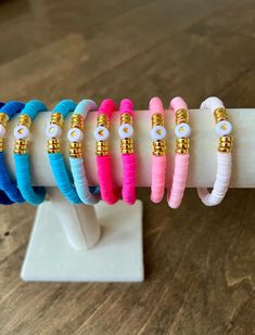 five bracelets with gold and blue beads are on a white display stand in front of a wooden table