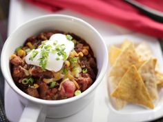 a white bowl filled with chili and cheese next to tortilla chips