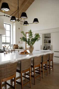 a large kitchen island with chairs around it and lights hanging from the ceiling over it