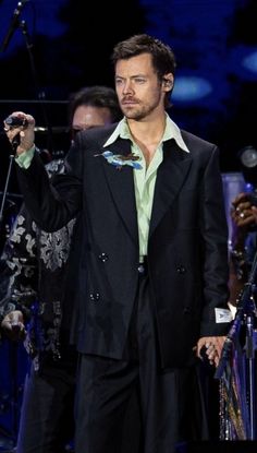 a man in a black suit and green shirt holding a microphone while standing on stage