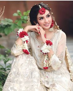 a woman in a white and red wedding outfit with flowers on her head sitting down