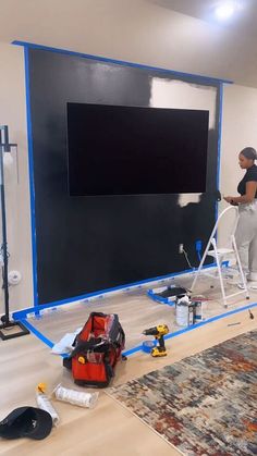 a woman standing on a ladder in front of a black wall with a large screen