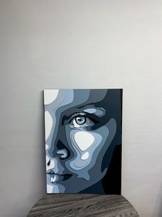 a painting of a woman's face on a wooden table next to a white wall