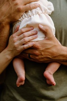 a close up of a person holding a baby in their arms with the other hand