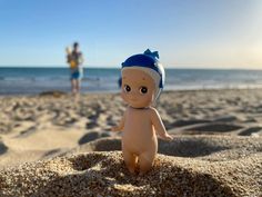 a small doll sitting on top of a sandy beach next to the ocean with people in the background