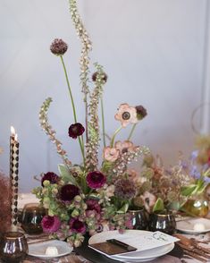 an arrangement of flowers and candles on a table with place settings for two people to sit at