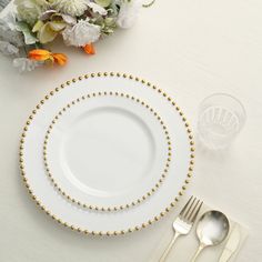 a white plate topped with gold beaded plates next to silverware and flowers on a table