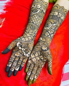 two hands that are decorated with henna designs on red fabric and green flowers in the background