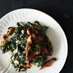 a white plate topped with spinach and bacon on top of a black tablecloth