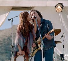 two people on stage with guitars and microphones in front of an open air tent