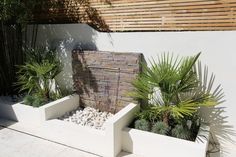 an outdoor fountain surrounded by plants and rocks in the middle of a patio area with wood slats