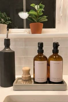 two bottles are sitting on a tray in front of a window with a brush and soap dispenser