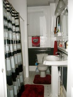 a bathroom with black and white striped shower curtain, rugs, sink and toilet