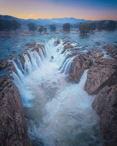 an aerial view of a waterfall in the middle of some rocks and water at sunset