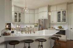 a kitchen with white cabinets and marble counter tops, stools in front of the island