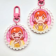 two pink and white keychains with cartoon characters on them, one is holding a cell phone