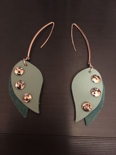 two pairs of earrings with green leaves and gold buttons on them, sitting on a table