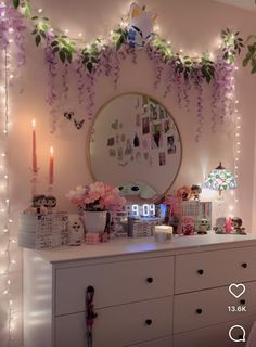 a dresser with flowers and candles on it in front of a wall decorated with lights