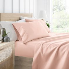 a bed with pink sheets and pillows on top of it next to a night stand