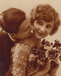 an old black and white photo of two women hugging each other with flowers in their hands