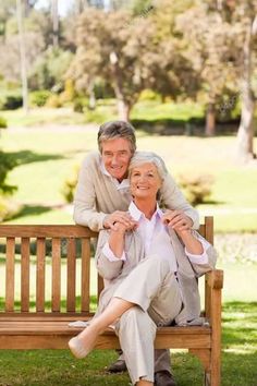 an older couple sitting on a wooden bench in the park, posing for a photo