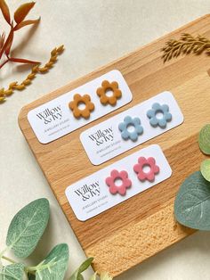 three flower shaped magnets sitting on top of a wooden board next to green leaves