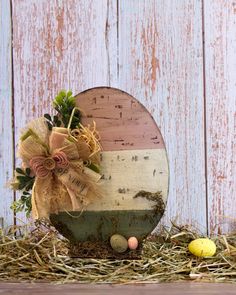 an easter basket with eggs and flowers in front of a painted wooden fence, next to straw bales