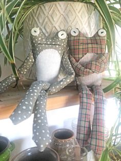 two stuffed animals sitting next to each other on top of a shelf near potted plants