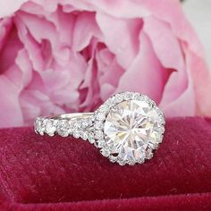 a diamond ring sitting on top of a red velvet box next to a pink flower