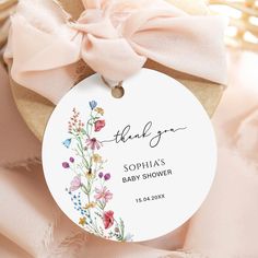 a baby shower tag with flowers on it and a pink ribbon tied around the tag