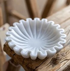 a white bowl sitting on top of a wooden table next to a piece of wood